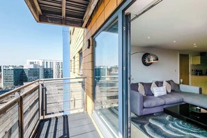 A modern balcony with a glass railing, a sofa, and a dining table.