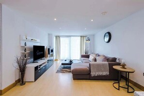 A modern living room with a flat-screen TV, a sofa, a coffee table, and a small side table.