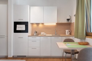 Een moderne keuken met witte kasten, een ingebouwde oven, een koffiezetapparaat en een eethoek met een tafel en stoelen.