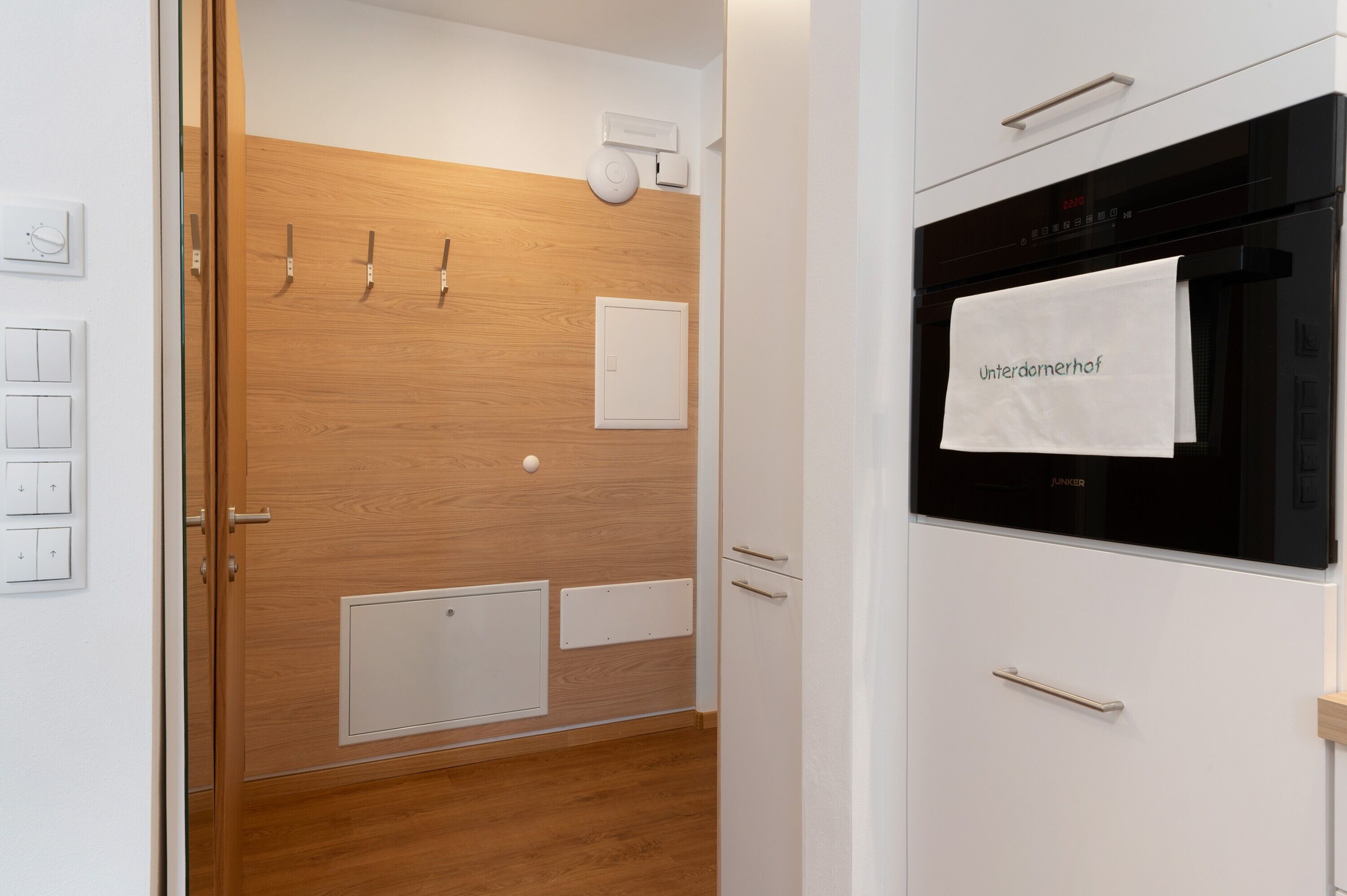 Una cucina moderna con un forno JUKER, pannello di legno a parete e un asciugamano appeso al manico del forno.