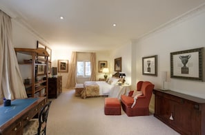 A hotel room with a bed, a desk with a chair, a red armchair, a wooden cabinet, and framed artwork on the walls. - Sunset Luxe Retreat (San Bartolomé de Tirajana)