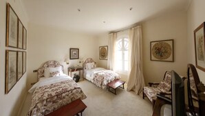 Ein Schlafzimmer mit zwei Betten, einem kleinen Tisch, einem Stuhl, einem Fernseher und gerahmten Bildern an den Wänden.