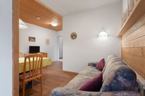 A room with a wooden ceiling, a sofa with cushions, a chair, a TV, and a small table.
