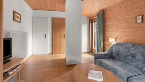 A room with a wooden ceiling, a sofa, a television, a door, and a window with curtains.