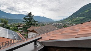 A view from a balcony with a metal railing, a solar panel, and a mountain landscape in the background.