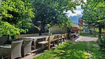 Une terrasse extérieure aménagée avec des meubles en bois et une table, entourée de verdure et offrant une vue sur les montagnes.