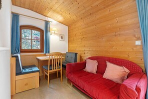 A cozy room with a wooden ceiling, a red sofa, a wooden bench, a table, and a window with curtains.