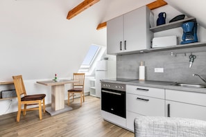 Une cuisine moderne dotée d’un four encastré, d’un coin repas avec une table et des chaises, et d’une fenêtre laissant entrer la lumière naturelle.