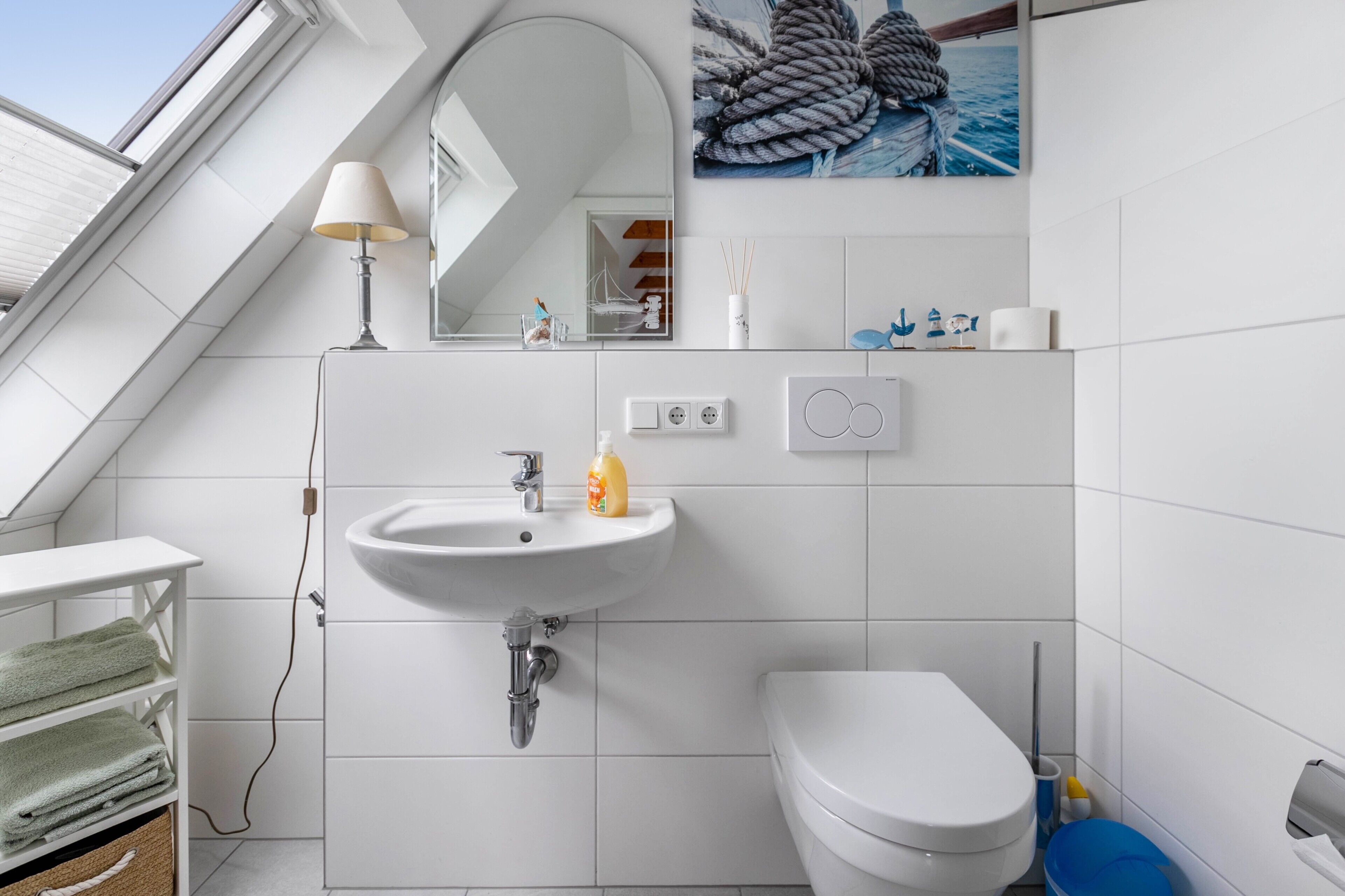 A modern bathroom with a skylight, white tiles, a sink, a toilet, and a mirror.
