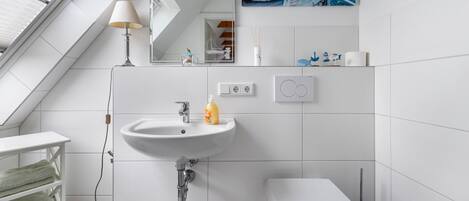 A modern bathroom with a skylight, white tiles, a sink, a toilet, and a mirror.