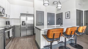 A modern kitchen with stainless steel appliances, a central island with bar stools, and a large window providing natural light.