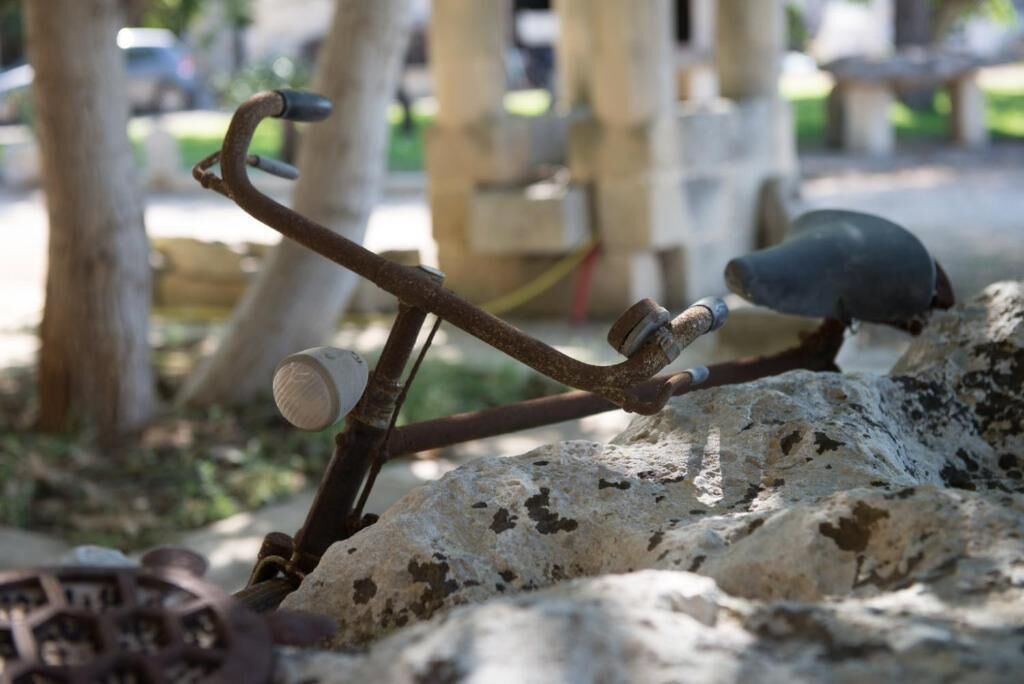 A rustic metal structure with a bird perched on it, set against a natural backdrop with trees and a stone wall.