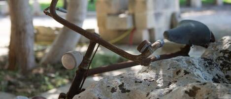 A rustic metal structure with a bird perched on it, set against a natural backdrop with trees and a stone wall.