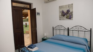 A bedroom with a bed, a nightstand, a lamp, and a door leading to an outdoor area. - Villa dei Bruno (San Donato di Lecce)