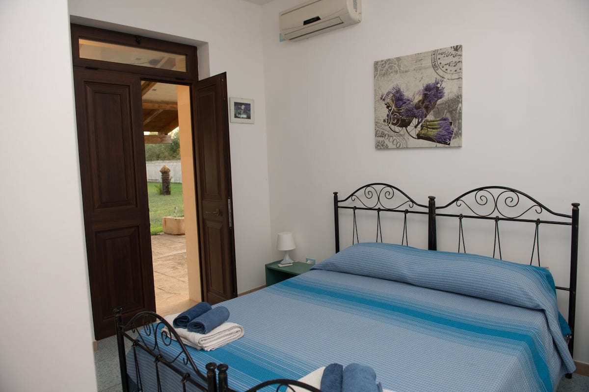 Un dormitorio con cama, mesita de noche, lámpara y puerta que da a un espacio exterior.