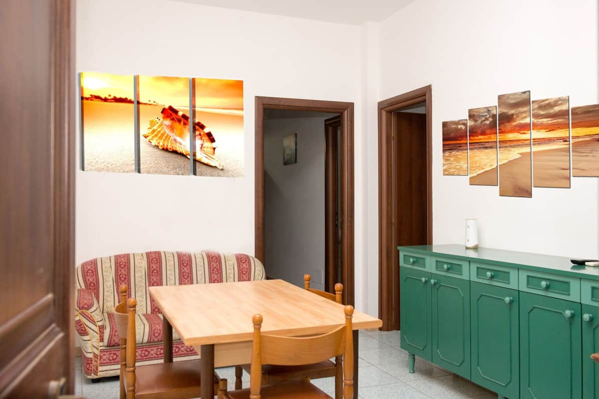 Un comedor con una mesa y sillas de madera, un armario verde y un sofá con cojines estampados.