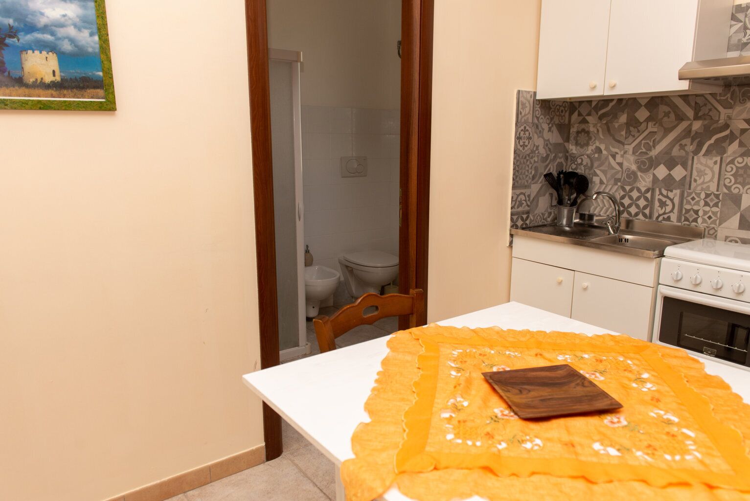 A small kitchen with a white table, a wooden chair, and a painting on the wall.