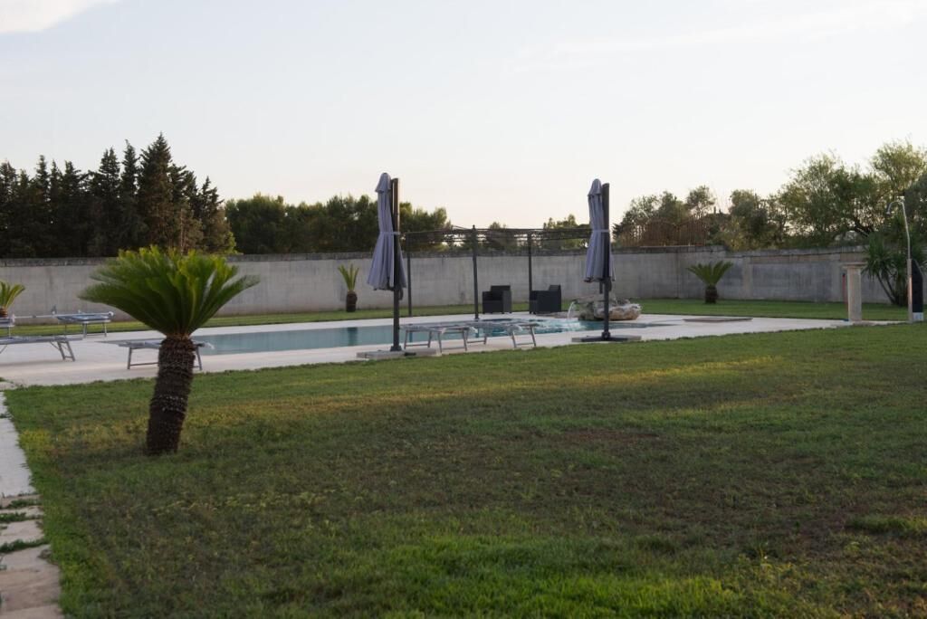 A pool area with lounge chairs and umbrellas, surrounded by grass and trees.