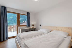 Een slaapkamer met twee bedden, een bureau, een stoel en uitzicht op een balkon.