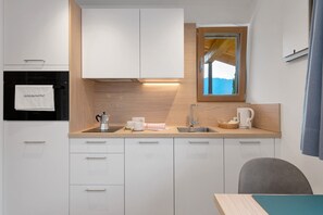 Een moderne keuken met witte kasten, een inbouwoven, een raam met uitzicht en een spoelbak met waterkoker.