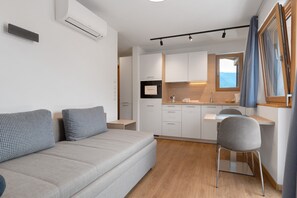 Una habitación moderna con sofá, sillón, kitchenette y ventana con cortinas.