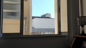 A room with a large window, a view of buildings outside, and a lamp on a table.