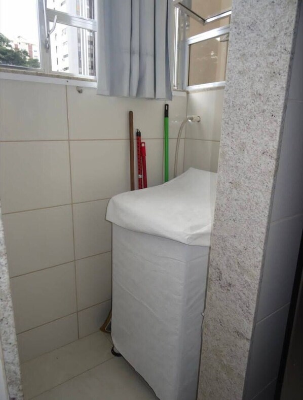 A small, tiled bathroom with a white sink, a mirror, and a window with curtains.