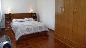A bedroom with a wooden bed, two bedside tables with lamps, a wardrobe, and a washing machine.