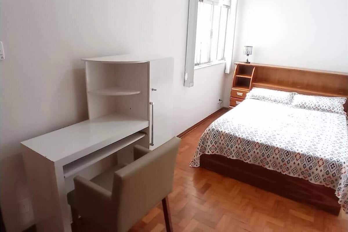 Un dormitorio con cama, escritorio con cajones, ventana y piso de madera.