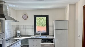 A compact kitchen with white cabinets, a built-in dishwasher, a coffee maker, and a window with a view of greenery. - Villa Over the 5th Green (San Bartolomé de Tirajana)