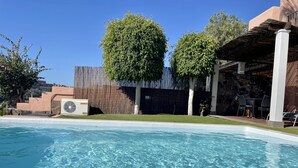 A swimming pool with clear water, surrounded by a wooden fence, a stone wall, and a covered patio area with chairs. - Villa Over the 5th Green (San Bartolomé de Tirajana)