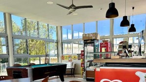 Amplio espacio interior con mesas y sillas, mesa de billar y grandes ventanales con vistas al exterior.