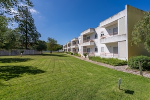 A row of modern, multi-story buildings with balconies, a well-maintained lawn, and a clear blue sky.