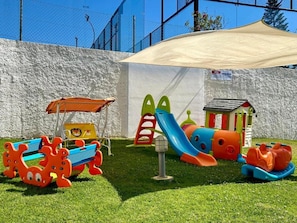 Un espace de jeux pour enfants avec un toboggan, une structure d’escalade et une petite maison.
