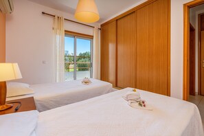 Een hotelkamer met twee bedden, een raam met gordijnen, een houten garderobe en een lamp.