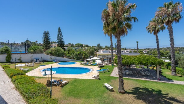 Un área de piscina con dos piscinas, palmeras y sillas de descanso.