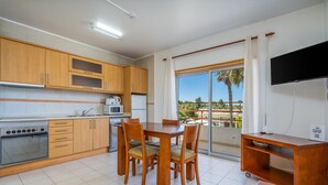 Una cocina moderna con armarios de madera, una mesa de comedor, sillas, un televisor y un balcón con vistas.