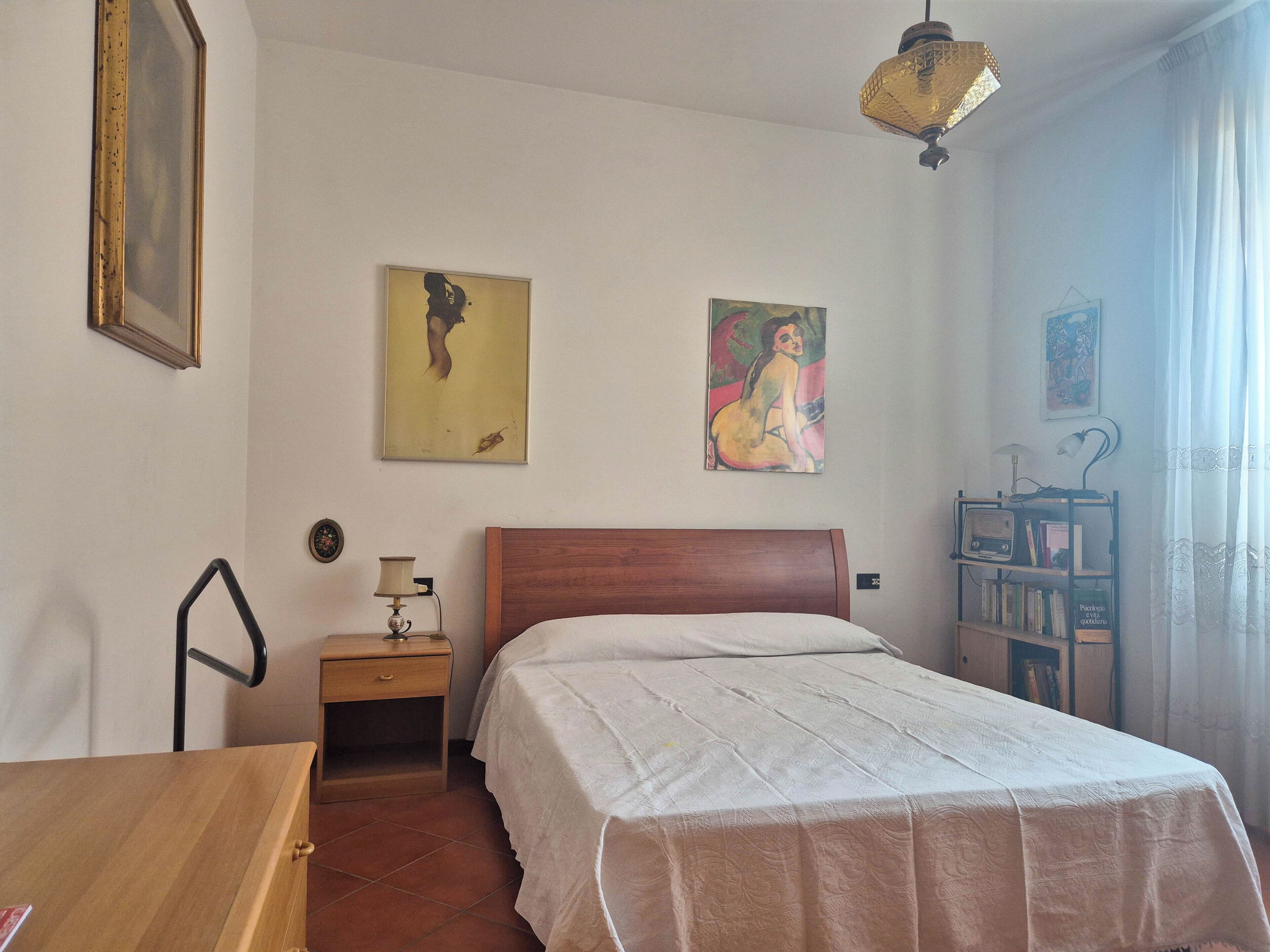Une chambre à coucher avec un lit en bois, une table de chevet avec une lampe, une chaise et deux tableaux accrochés au mur.