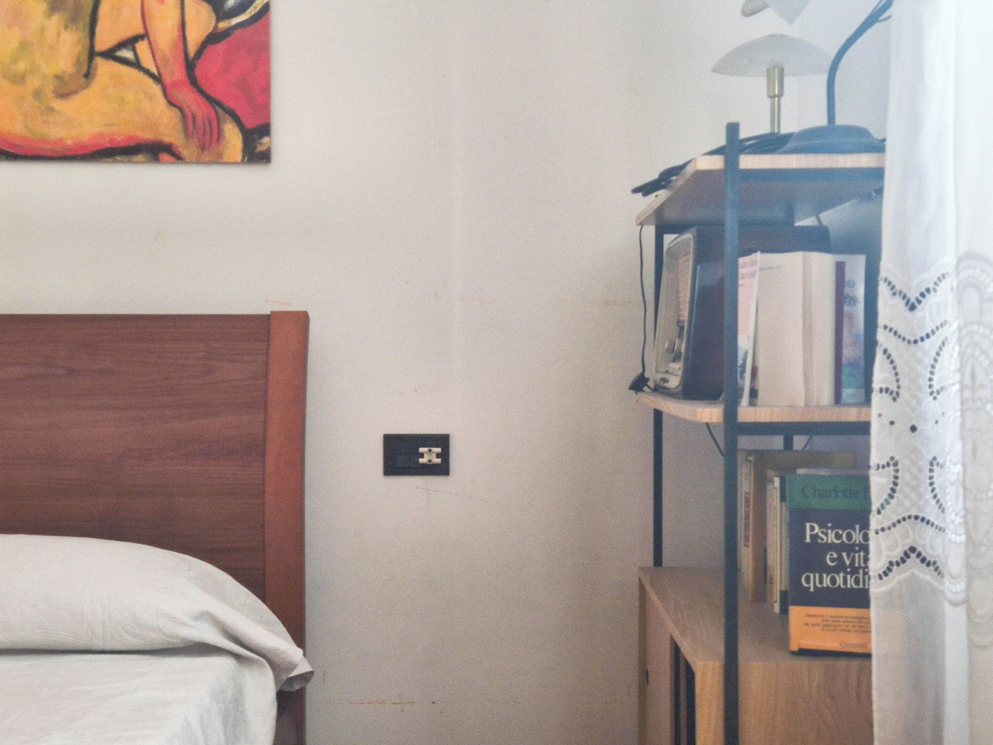 Un dormitorio con cabecera de madera, una mesita de noche, una lámpara y una estantería llena de libros.