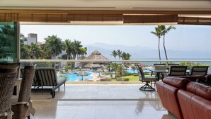 A balcony with a view of a resort pool, lounge chairs, and a leather sofa.