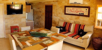 Uma sala de estar aconchegante com uma mesa de madeira, um sofá com mantas coloridas, uma televisão de tela plana na parede e um letreiro emoldurado sobre o sofá.