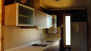 A compact kitchen with wooden cabinets, a built-in microwave, a water heater, and a refrigerator. - Casa Río Spa (San José)