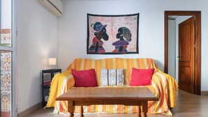A room with a sofa, a wooden table, a wall-mounted tapestry, and a door. - Brigth Apartment 'Macarena' with Balcony, Wi-Fi and Air Conditioning (Sevilla)
