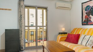 A room with a wooden table, a sofa with striped cushions, a sliding glass door, and a wall-mounted air conditioner. - Brigth Apartment 'Macarena' with Balcony, Wi-Fi and Air Conditioning (Sevilla)