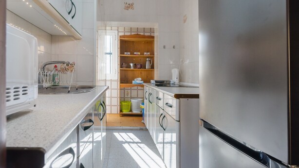 A modern kitchen with a stainless steel refrigerator, white cabinets, and a wooden shelf with kitchenware. - Brigth Apartment 'Macarena' with Balcony, Wi-Fi and Air Conditioning (Sevilla)