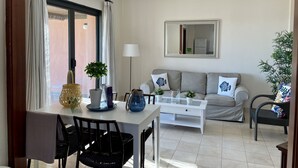 Een woonkamer met een bank, een salontafel, een eettafel met stoelen, een lamp en een spiegel aan de muur.