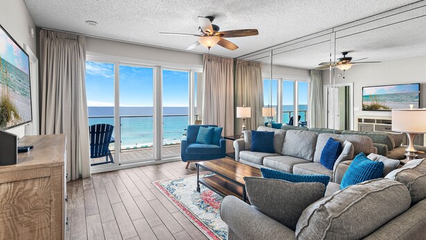 A spacious living area with a large window overlooking the ocean, a ceiling fan, and a modern fireplace.