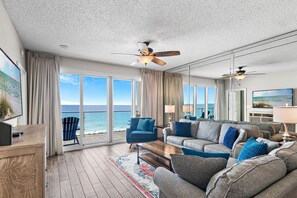 Een ruime woonkamer met een groot raam met uitzicht op de oceaan, een plafondventilator en een moderne open haard.