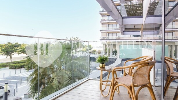 Ein Balkon mit Korbstühlen und einem kleinen Tisch, mit Blick auf eine Skyline mit Palmen und einer Straße.