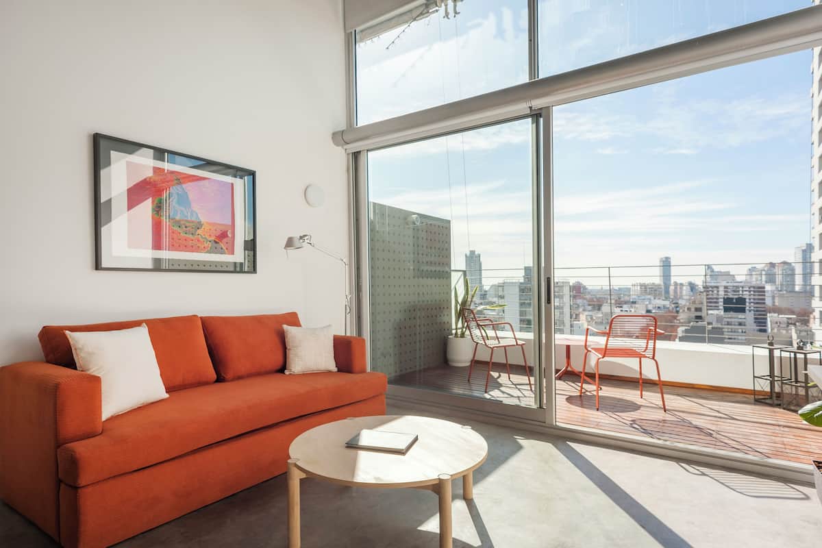 A modern living room with a red sofa, a round coffee table, and a large window offering a city view.